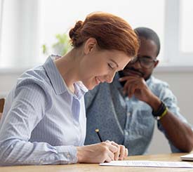 A man and woman sitting at a table signing papers to provide Proposal Support for a Federal Government agency through GSA.