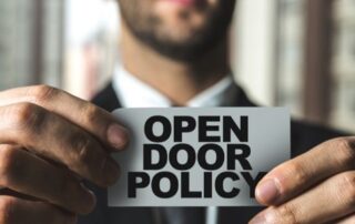 A businessman holding up a sign that says open door policy in the context of Proposal Support for the Federal Government. | Revolutionary Solutions A businessman holding up a sign that says open door policy in the context of Proposal Support for the Federal Government.