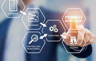 A man in a business suit is pointing at a project management icon, providing proposal support for the Federal Government. | Revolutionary Solutions A man in a business suit is pointing at a project management icon, providing proposal support for the Federal Government.