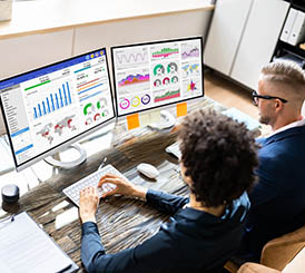 Two business people working at a desk with two monitors, providing GSA proposal support for the Federal Government.